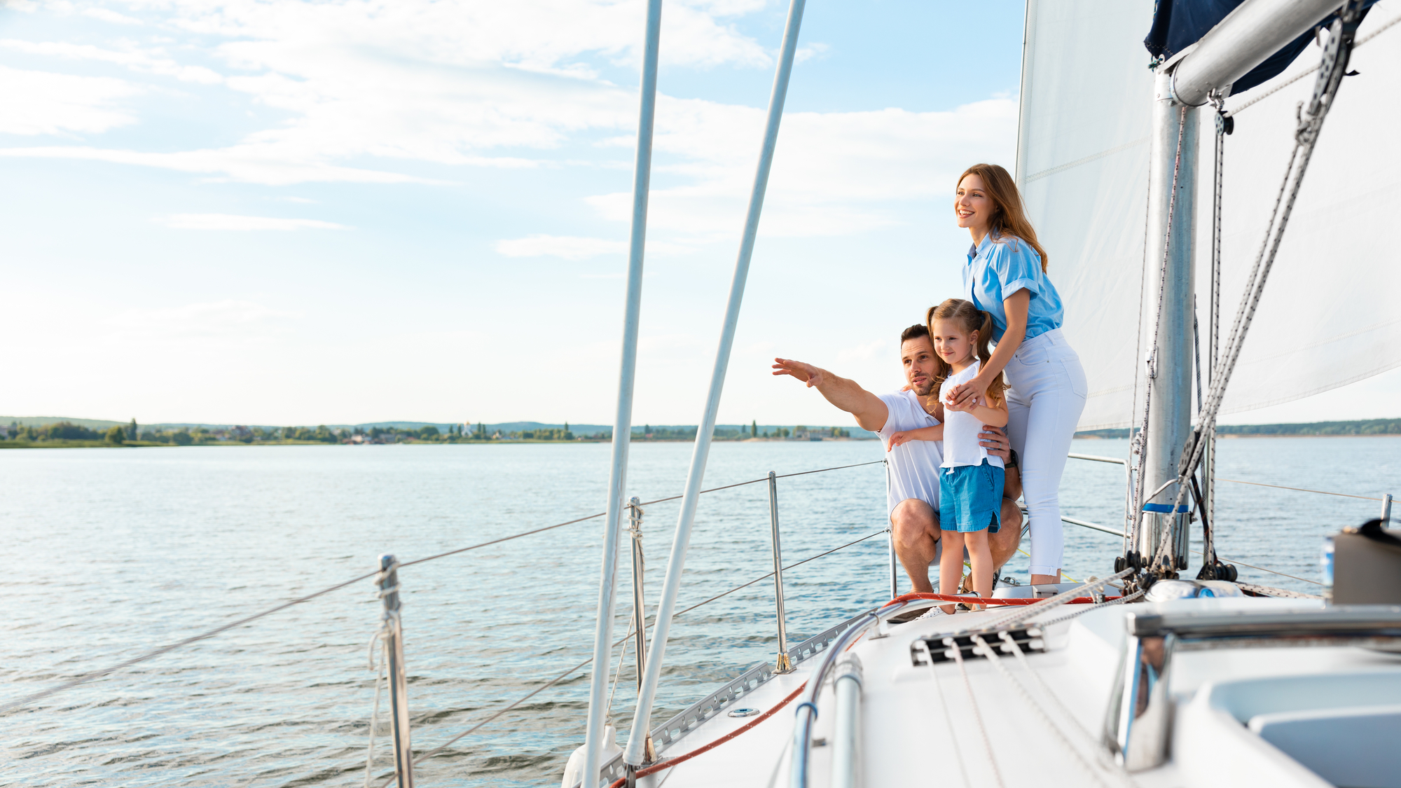Sailing. Happy Family Embracing Standing On Yacht Looking And Pointing Aside At Sea Water Outdoors. Parents And Daughter Relaxing On Sailboat Enjoying Summer Weekend Together. Panorama, Copy Space